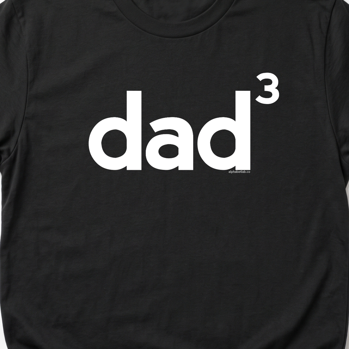 A black short-sleeve crewneck t-shirt with the word 'dad' printed in white lowercase letters, where the letter 'd' has a superscript '1' indicating 'first dad', shown on a light gray background.