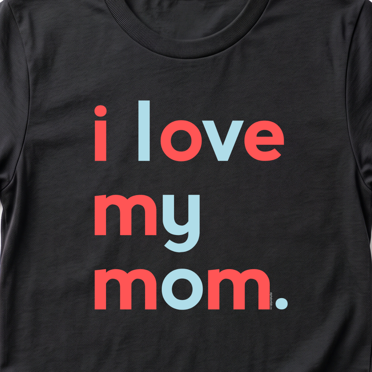 A black short-sleeve crewneck t-shirt with the phrase 'i love my mom.' printed on the front in a playful mix of coral red and light blue lowercase letters, shown against a plain white background.